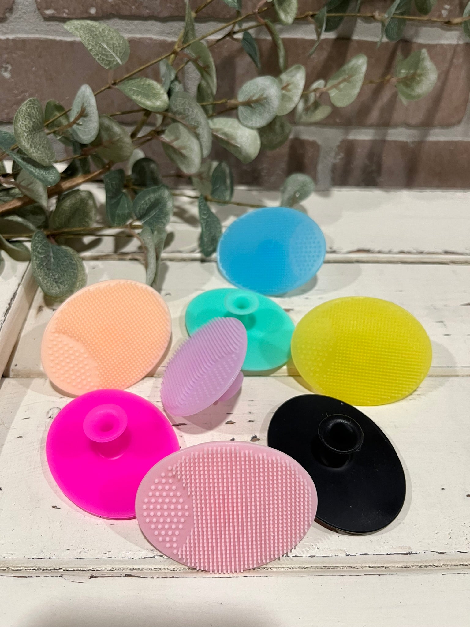 silicone face scrubbers in 8 different colors in front of brick wall